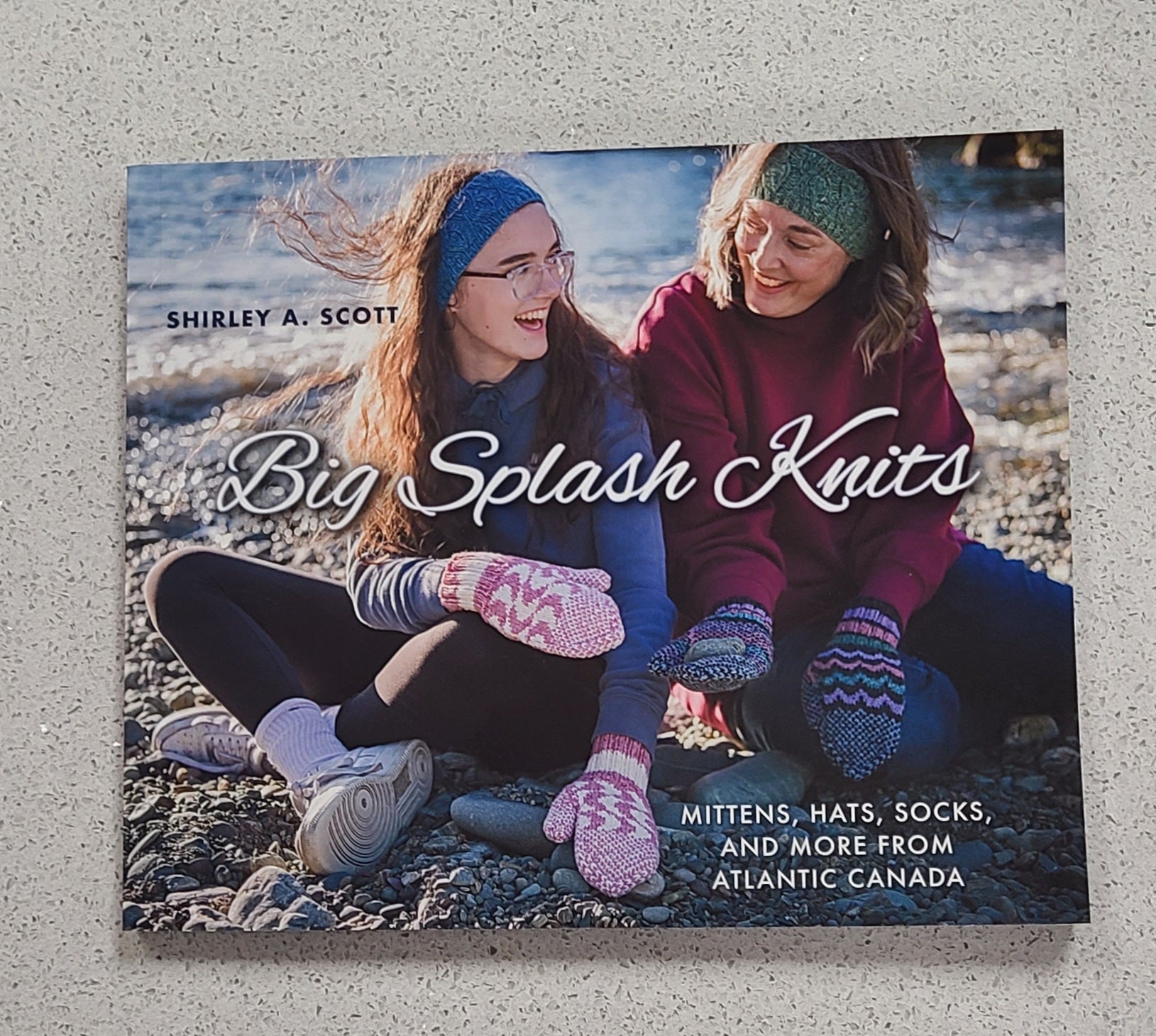 Book cover of 'Big Splash Knits' featuring two people sitting outdoors wearing knitted items.