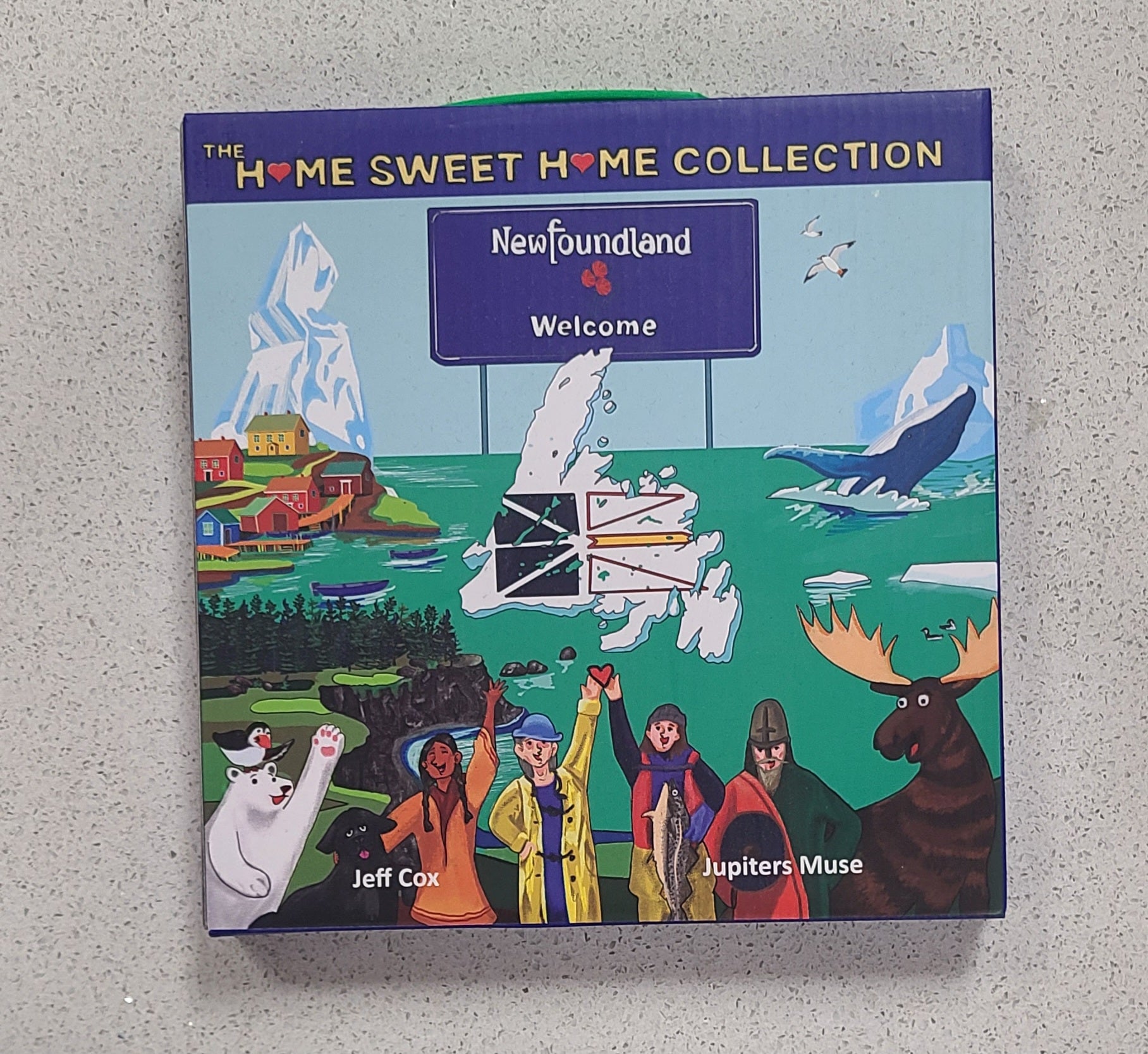 Book titled 'Home Sweet Home Collection: Newfoundland Welcome' by Jeff Cox and Jupiters Muse on a gray surface.