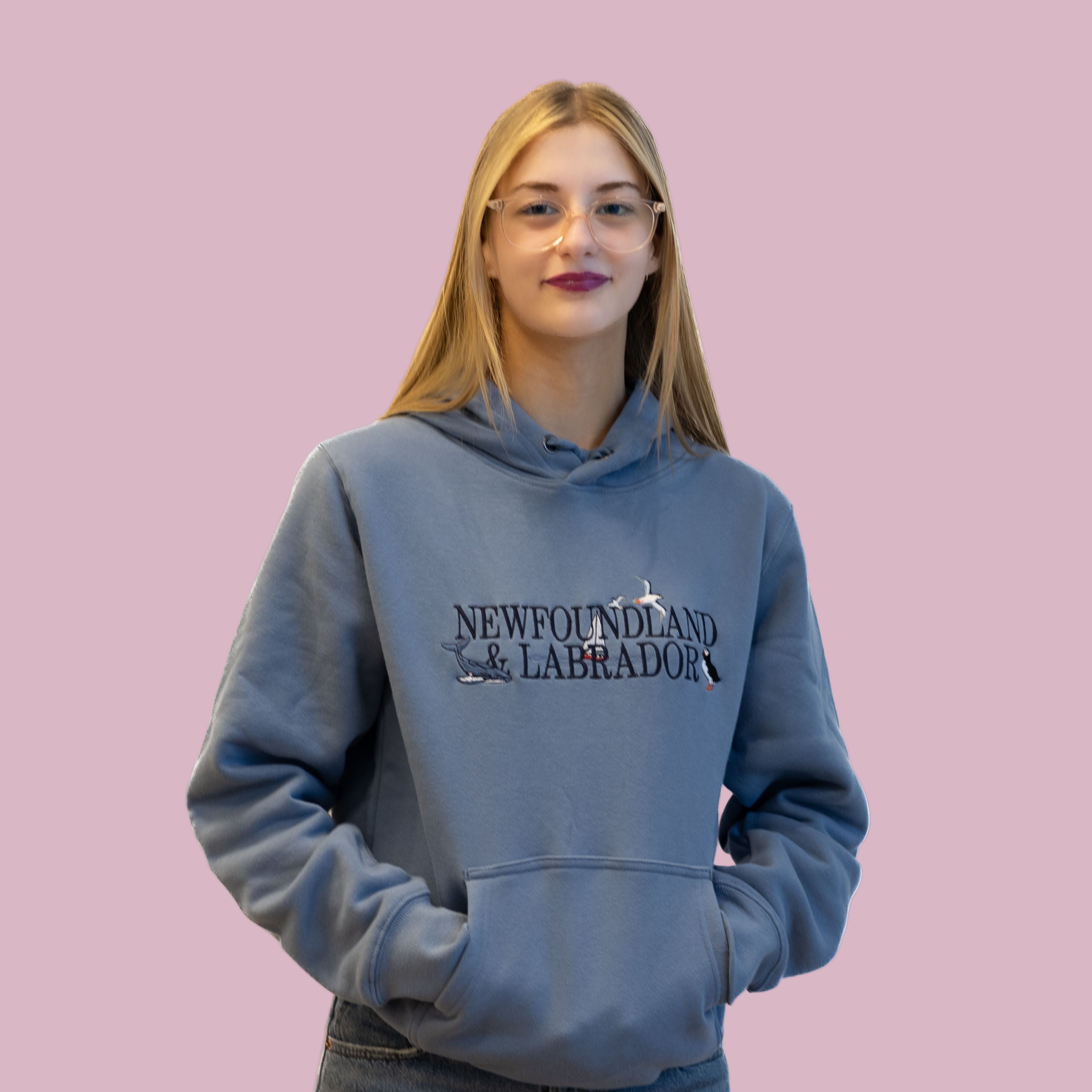 Young woman wearing a blue Coastal Newfoundland Hoodie with embroidered Newfoundland & Labrador design.