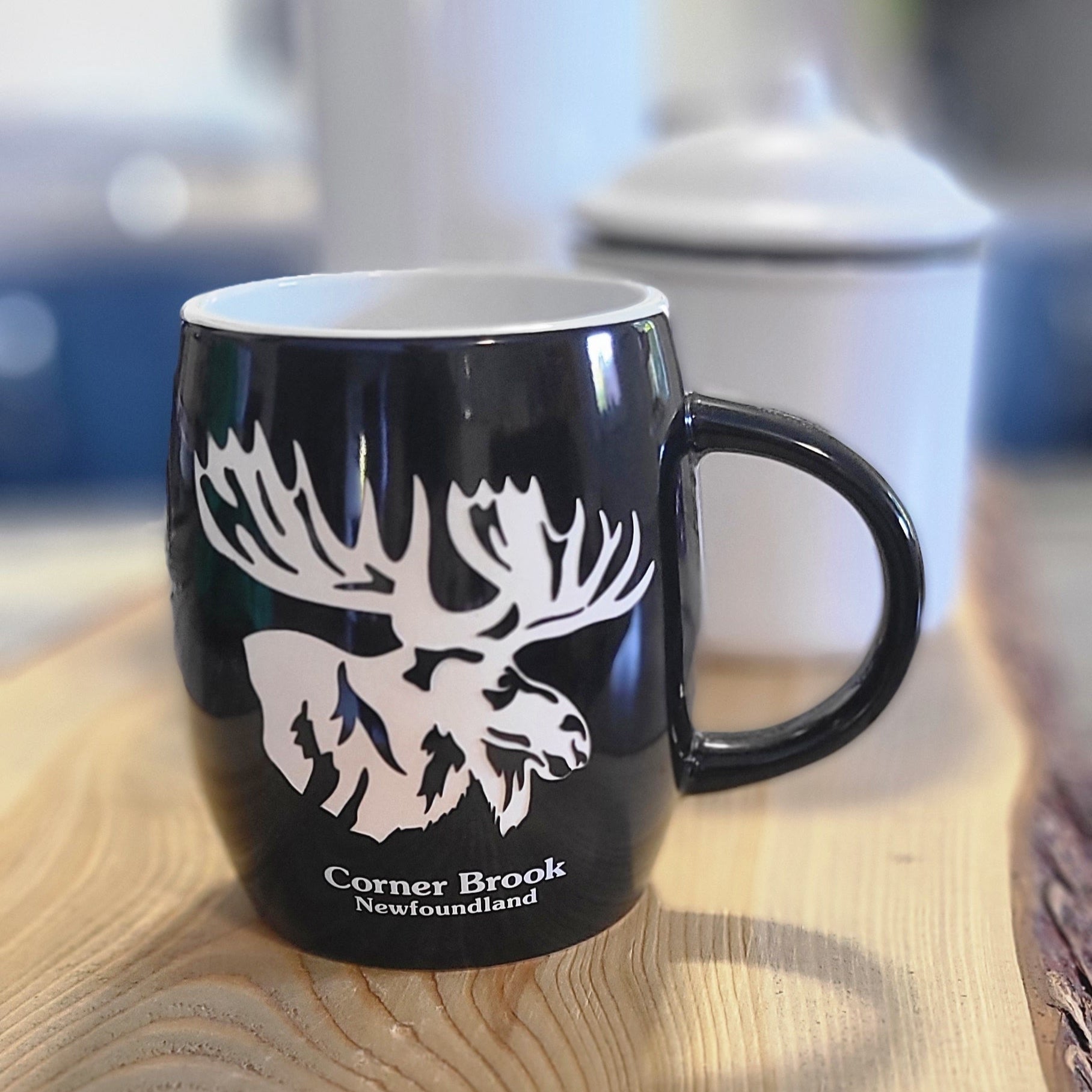 Ceramic mug with illustration of a moose, inspired by Corner Brook and Newfoundland wilderness, sitting on a wooden surface.