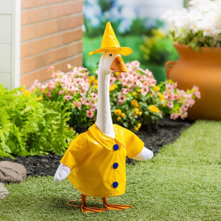 Toy duck in a yellow raincoat standing on grass with flowers in the background