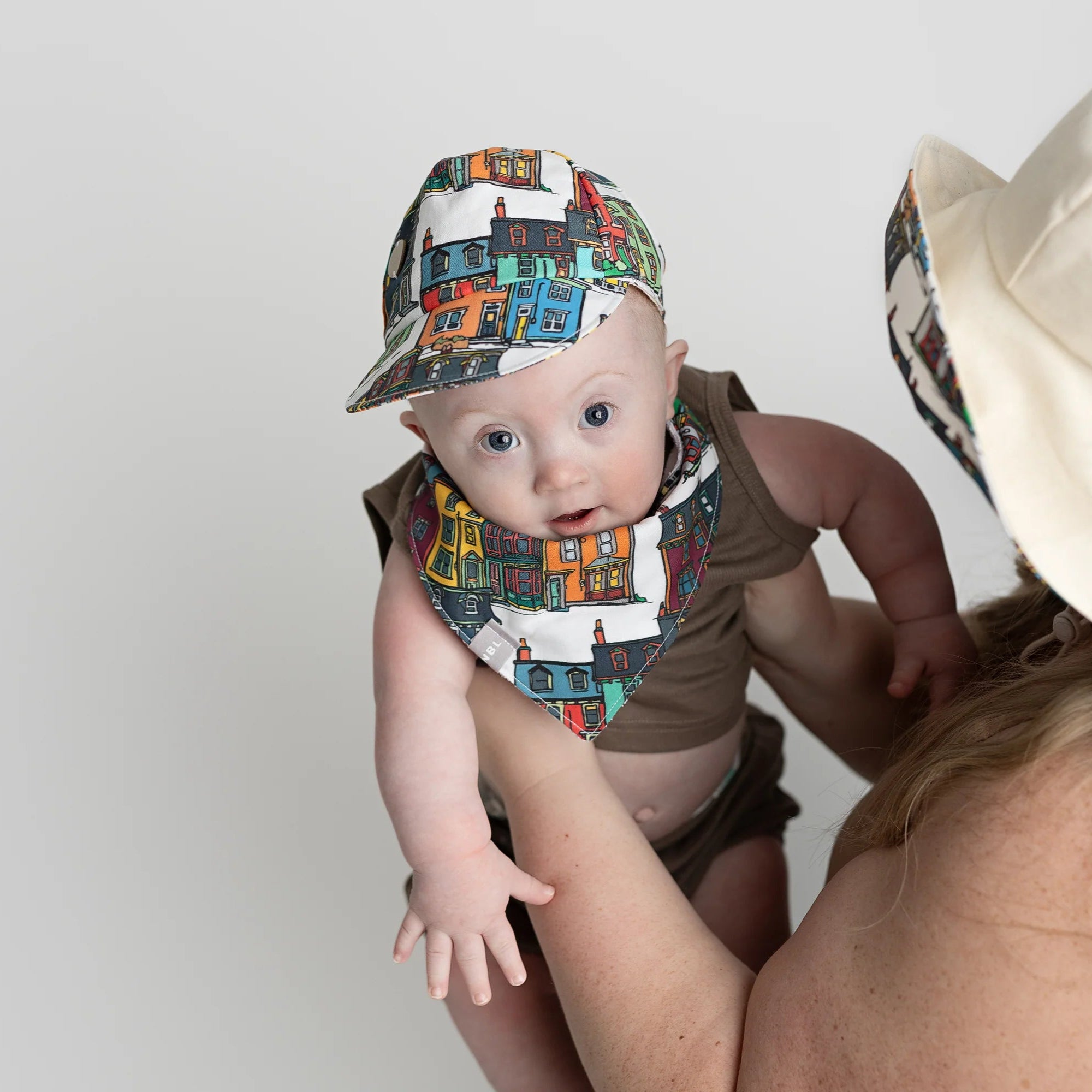 Baby wearing a colourful Jellybean Row Houses baseball cap and matching bib, inspired by St. John’s, Newfoundland.