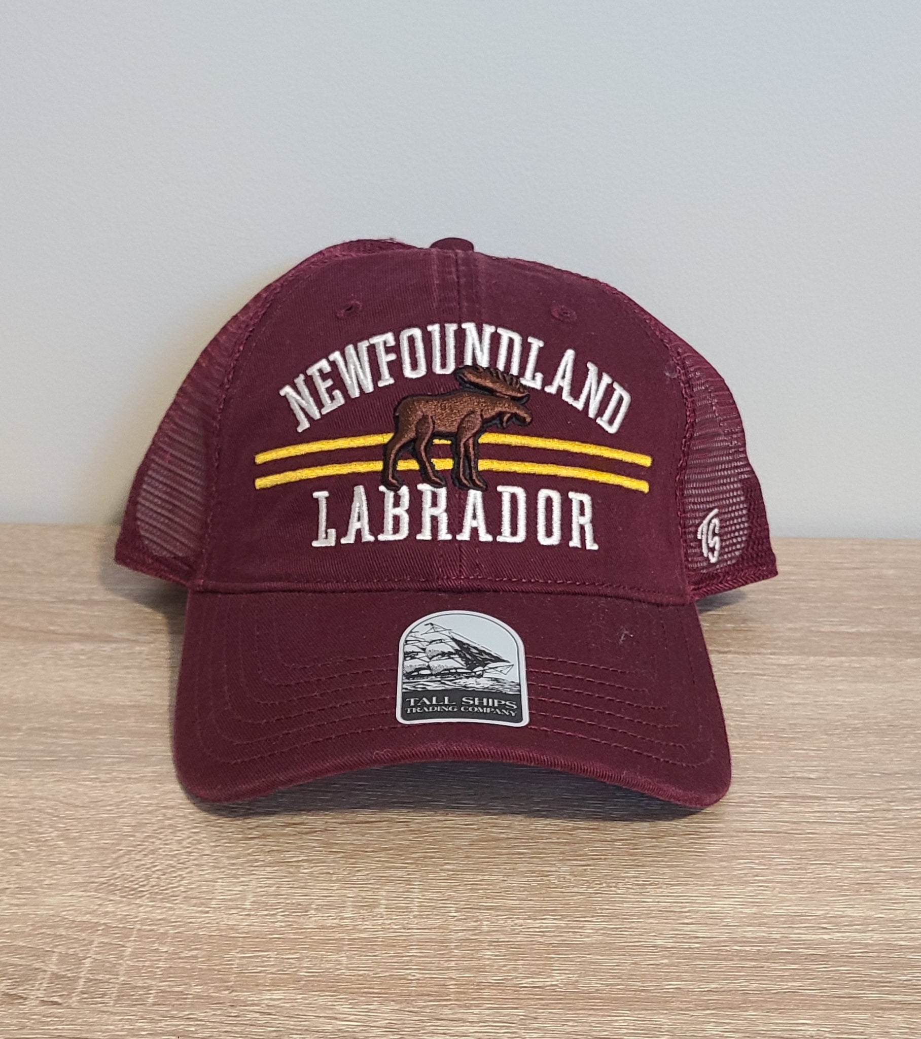 Maroon cap with 'Newfoundland Labrador' text on a wooden surface.