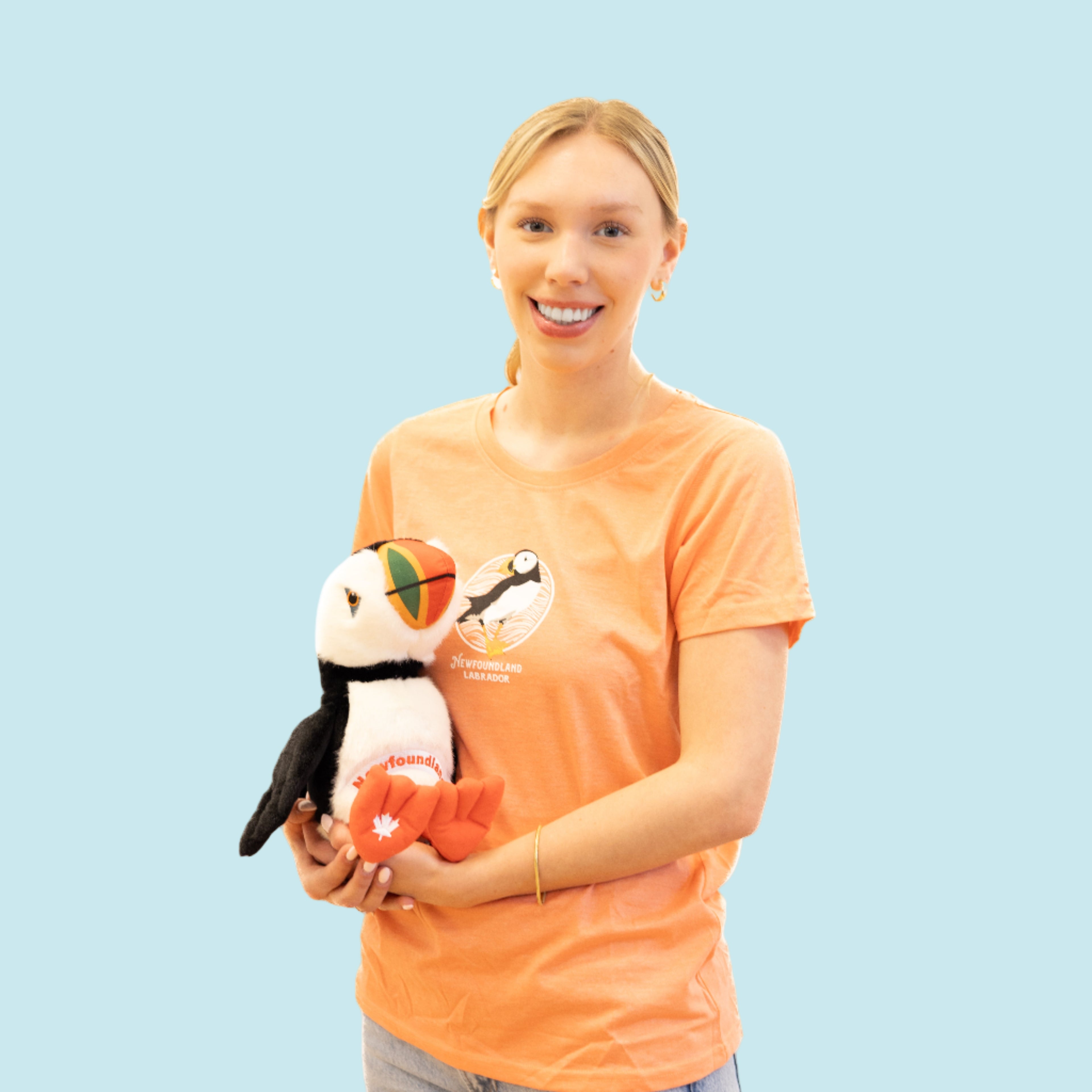Woman holding a plush Newfoundland puffin toy wearing an orange shirt with a puffin design.