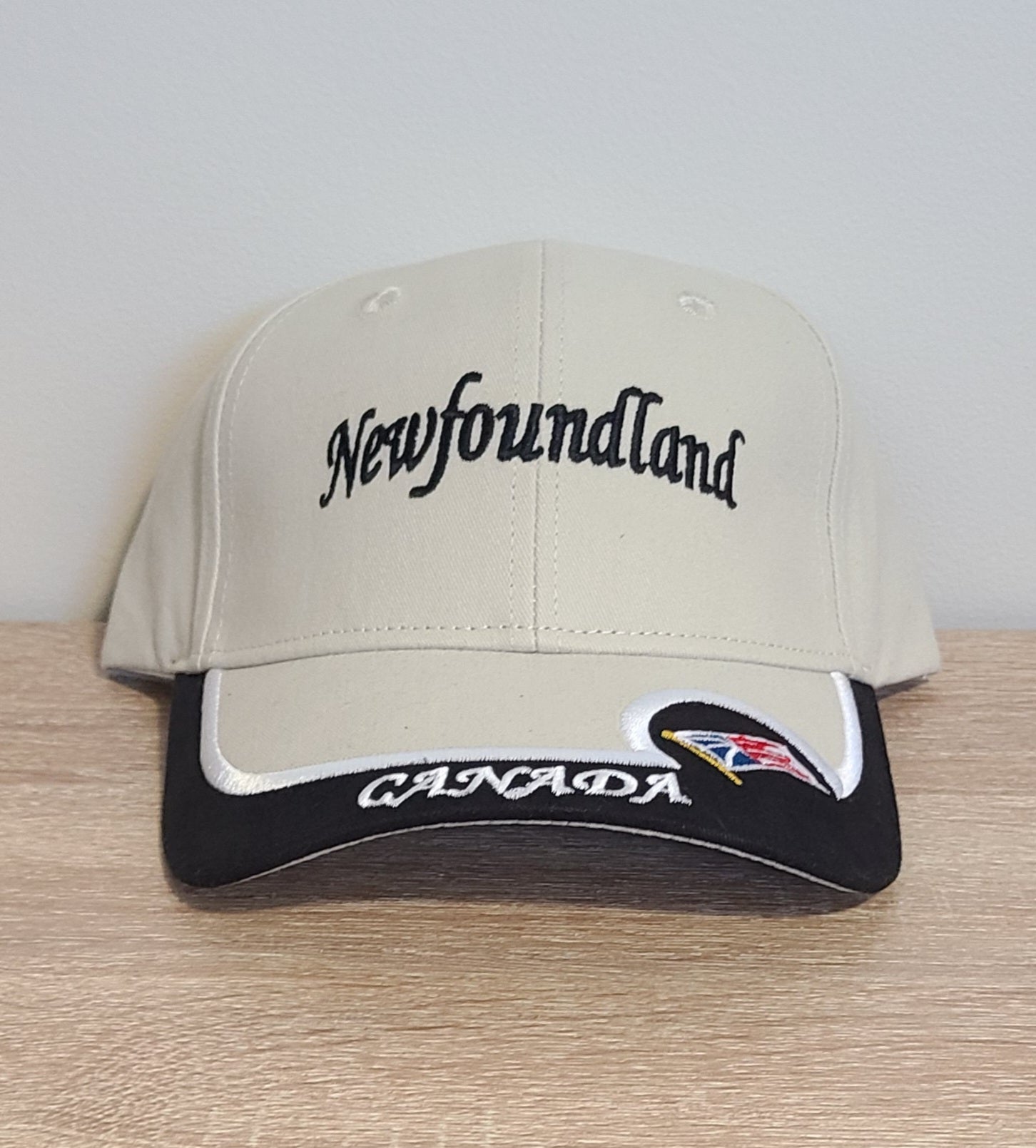 Beige cap with 'Newfoundland Canada' text and Newfoundland flag on a wooden surface