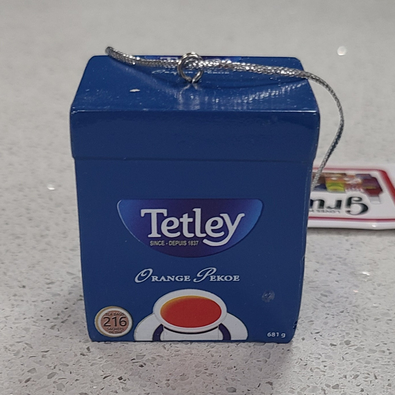 Blue Tetley Orange Pekoe tea box with a chain on a gray surface