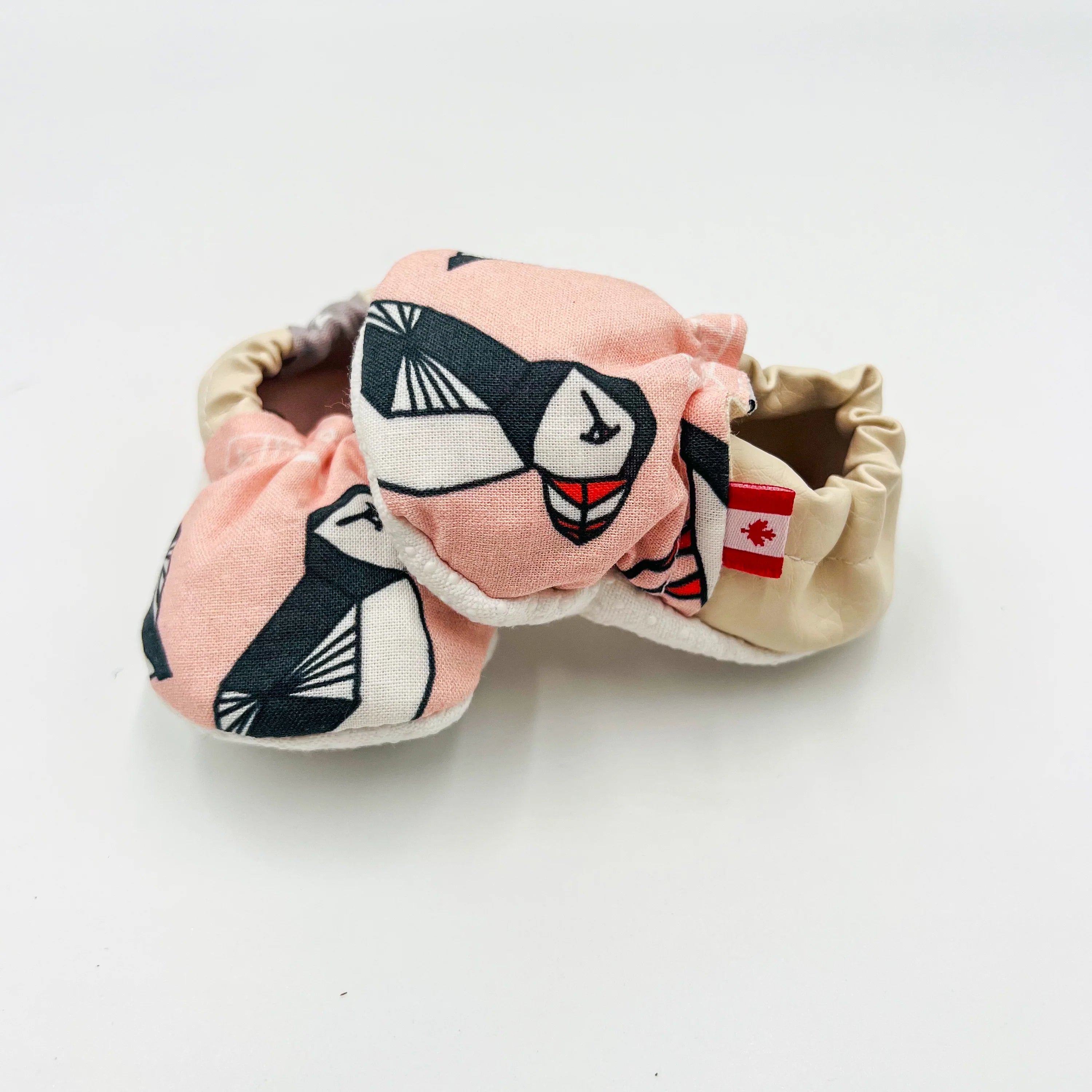 Pink Newfoundland puffin-print baby summer shoes with beige heel, antis-lip sole, Canadian flag tag, angled view showing side & front.