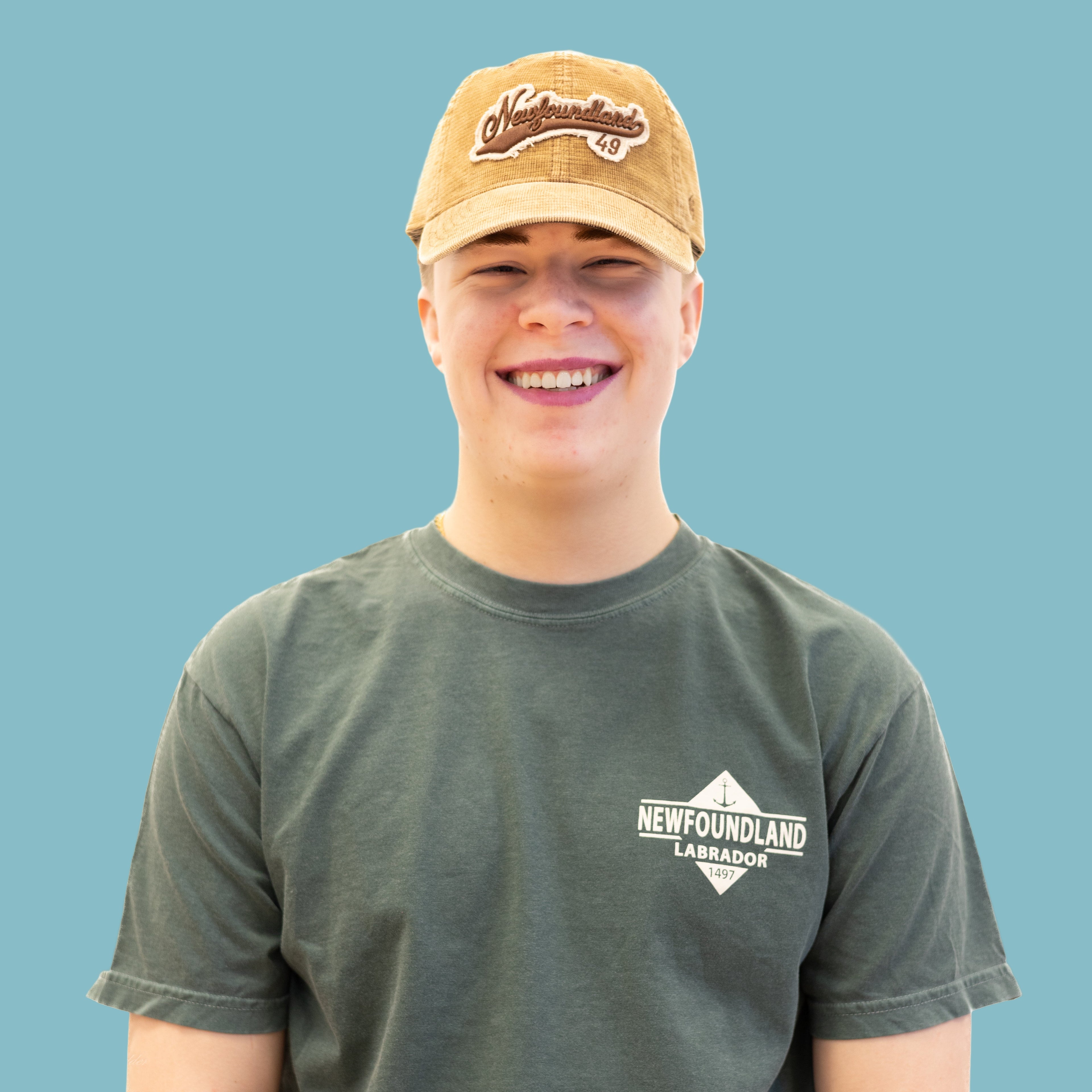 Smiling person wearing a tan Newfoundland 49 Baseball Hat with embroidered logo on the front.