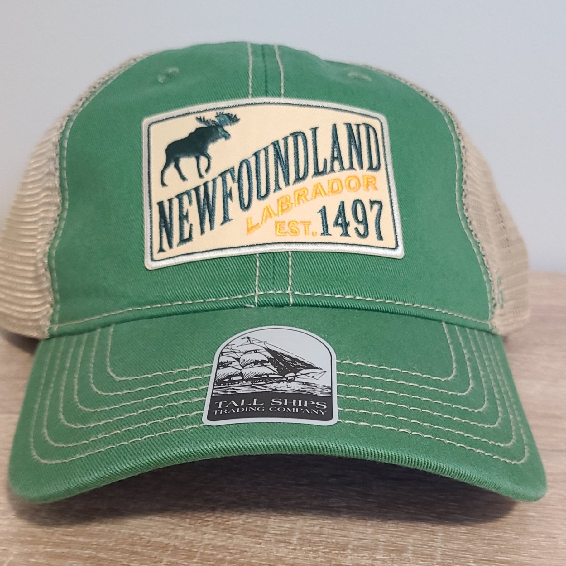 Front view of green Newfoundland Labrador EST. 1497 ball cap on a wooden surface.